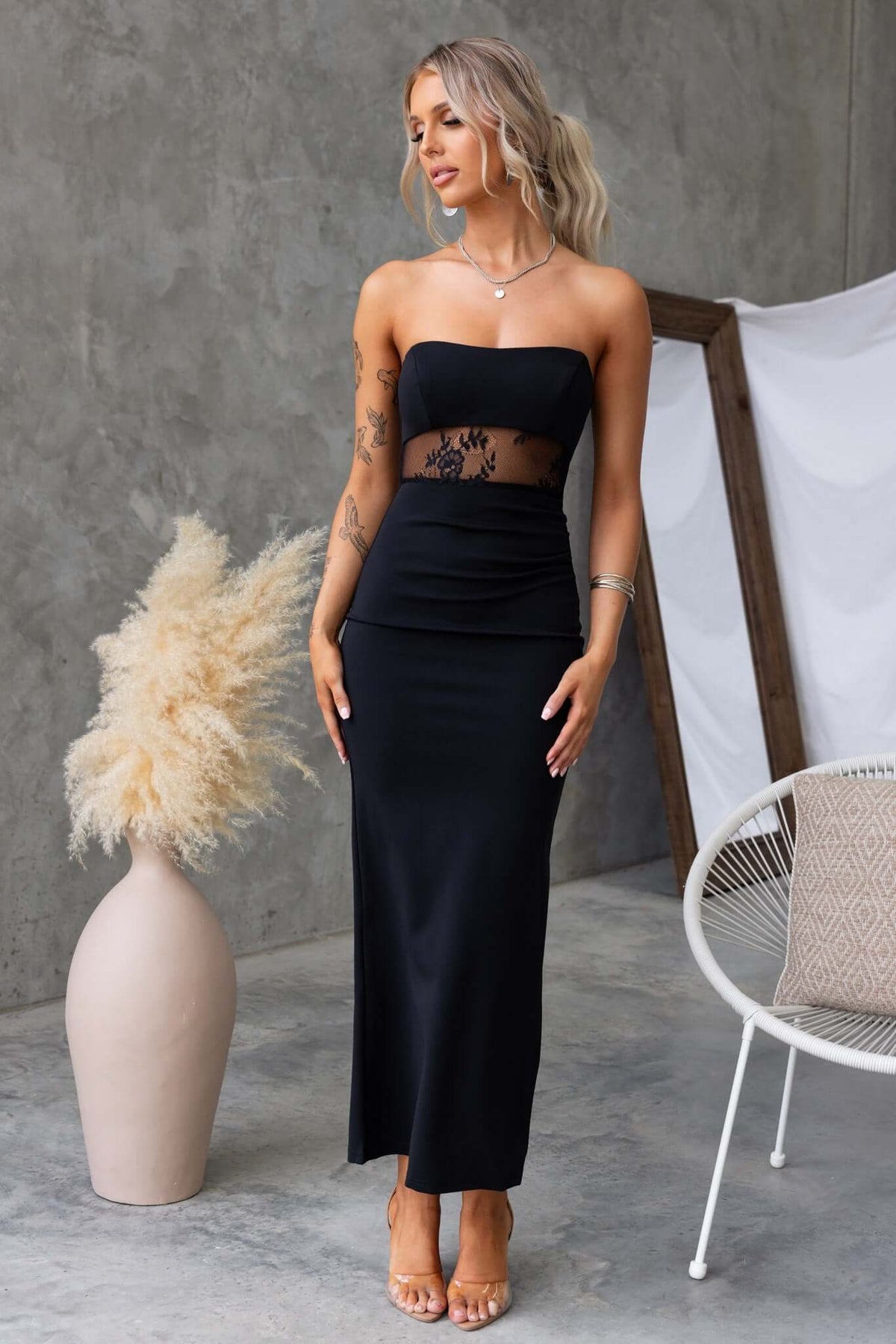 Model showcasing black Sassari maxi dress with strapless design and lace panel, perfect for elegant occasions.