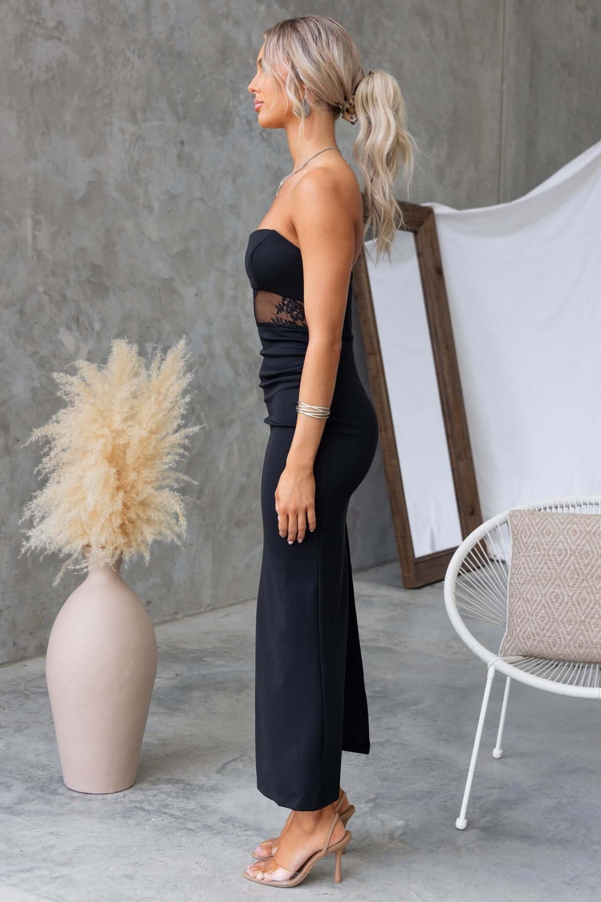 Elegant woman in a black Sassari maxi dress, showcasing a strapless design with lace details and a back split.