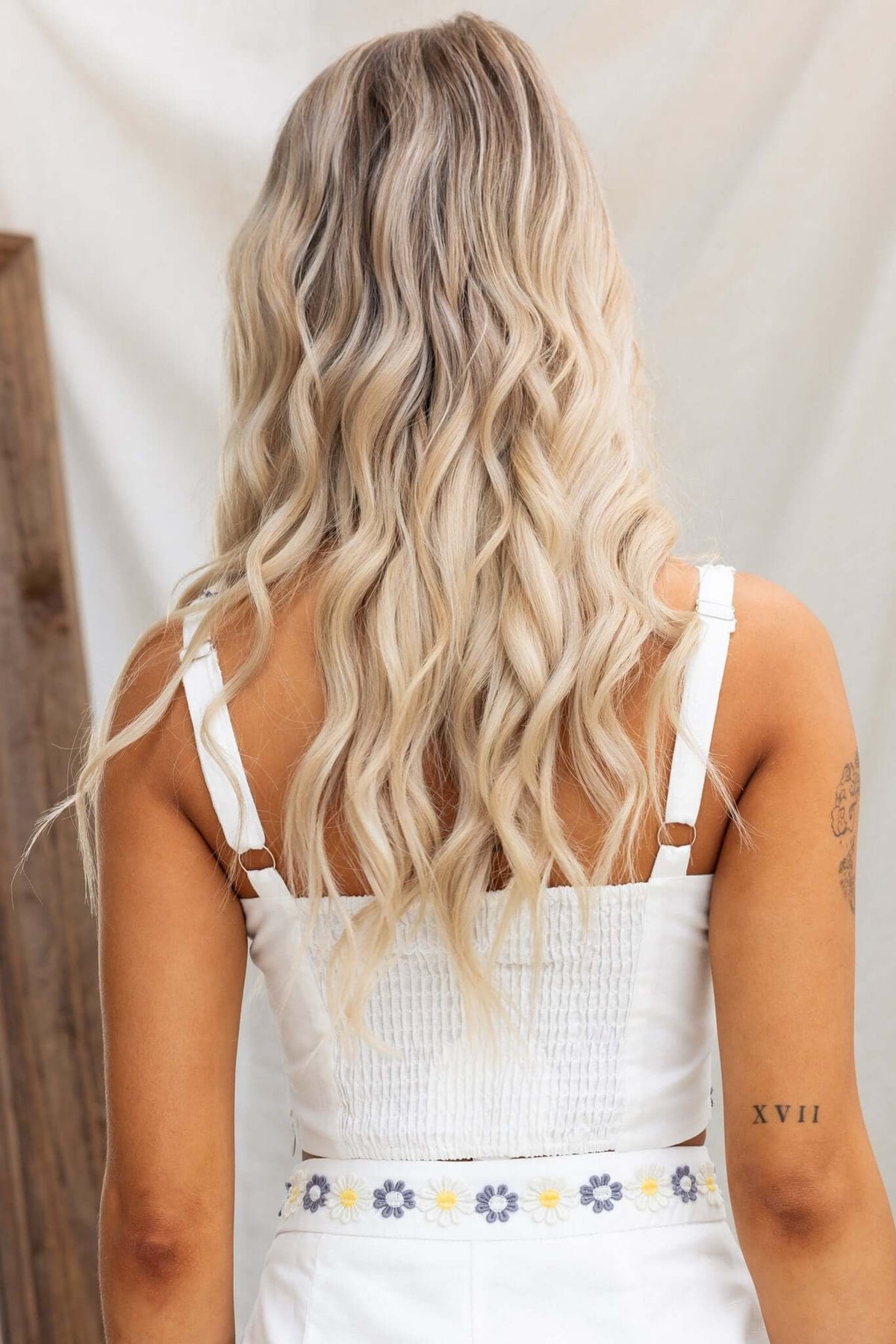 Back view of a woman in a white adjustable strap top, showcasing a textured design and wavy blonde hair.