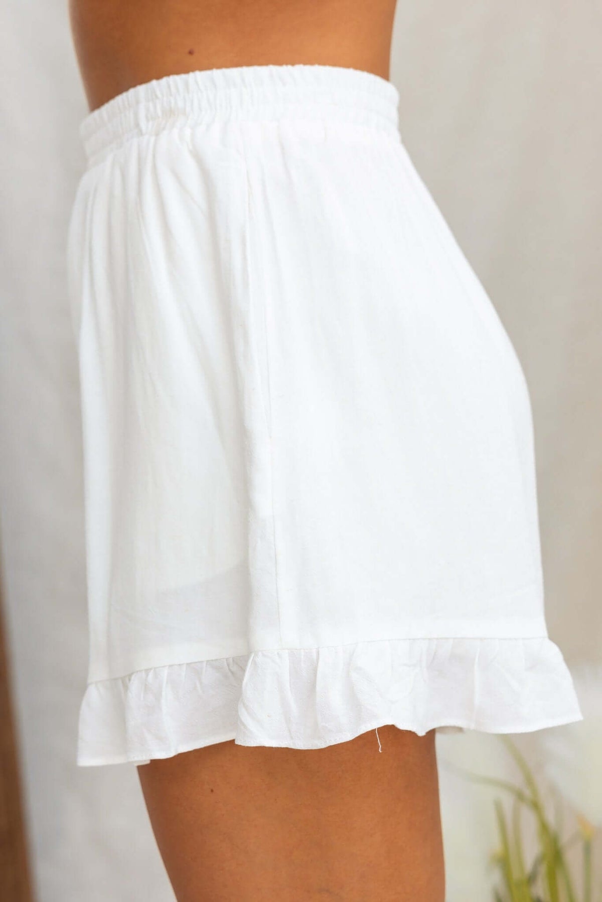 Side view of Mayok white shorts with ruffle hem and elastic waistband, perfect for warm weather.