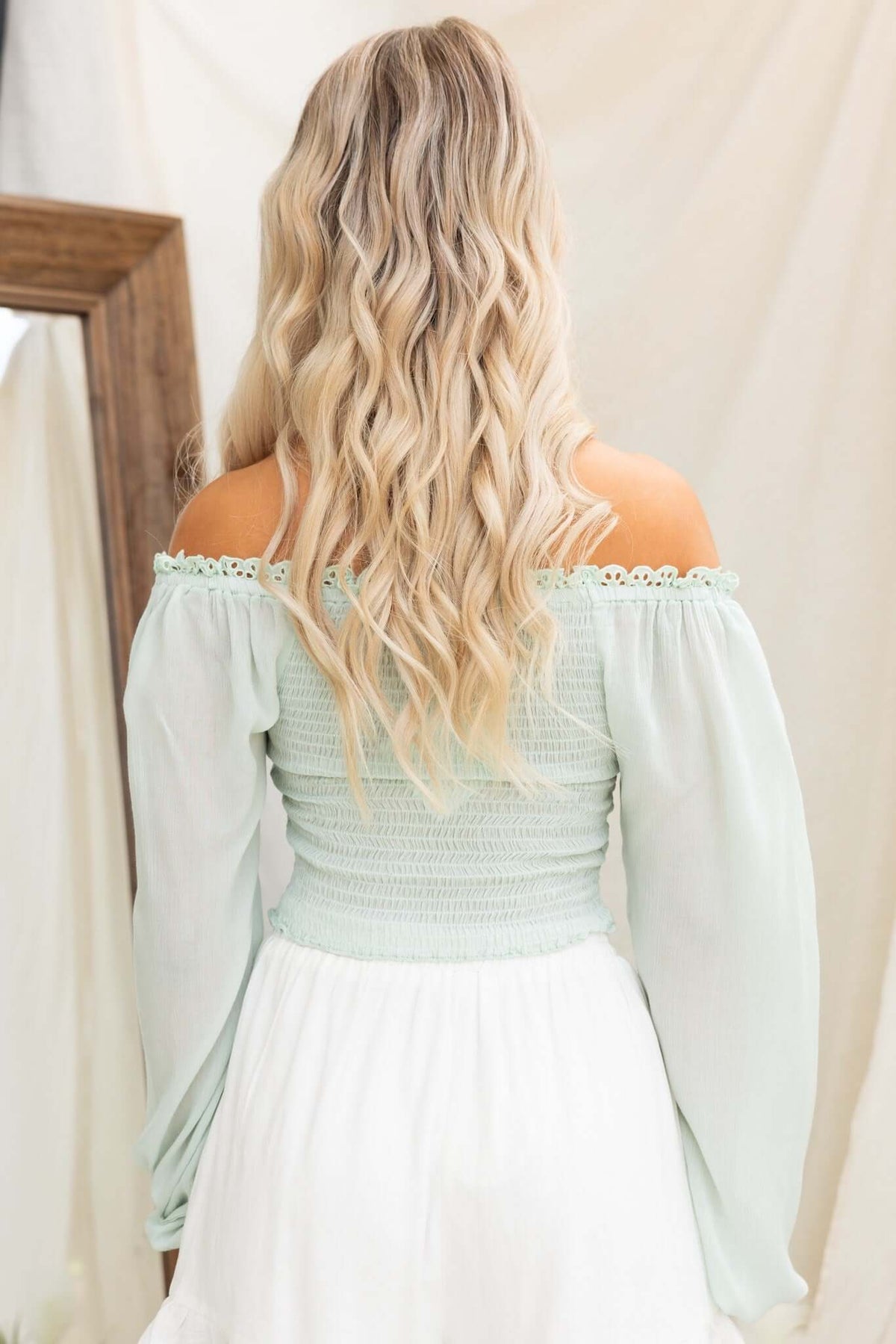 Back view of a woman in a mint green off-shoulder top with smocked detail and flowing sleeves.