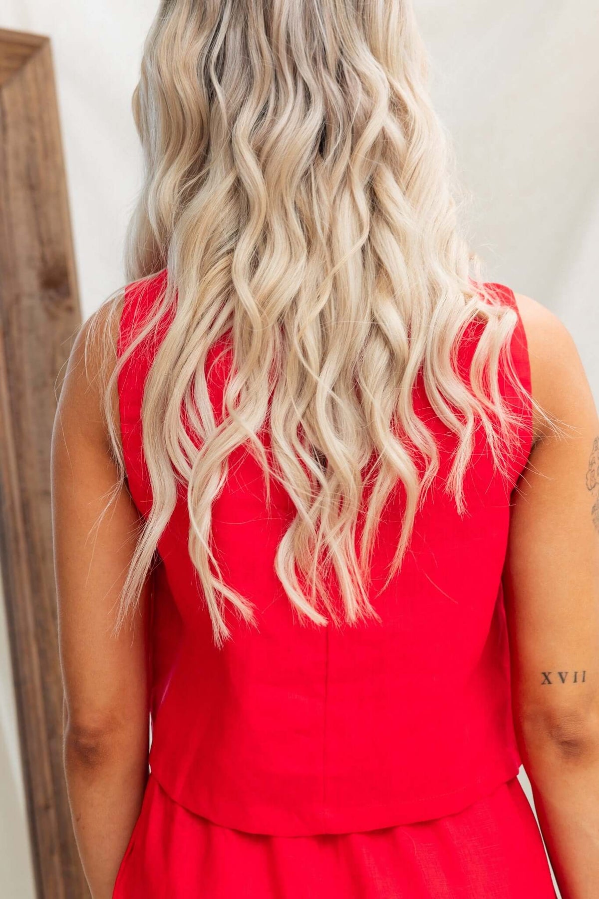Back view of a woman with wavy blonde hair wearing a vibrant red Orson Top, showcasing the button detail.
