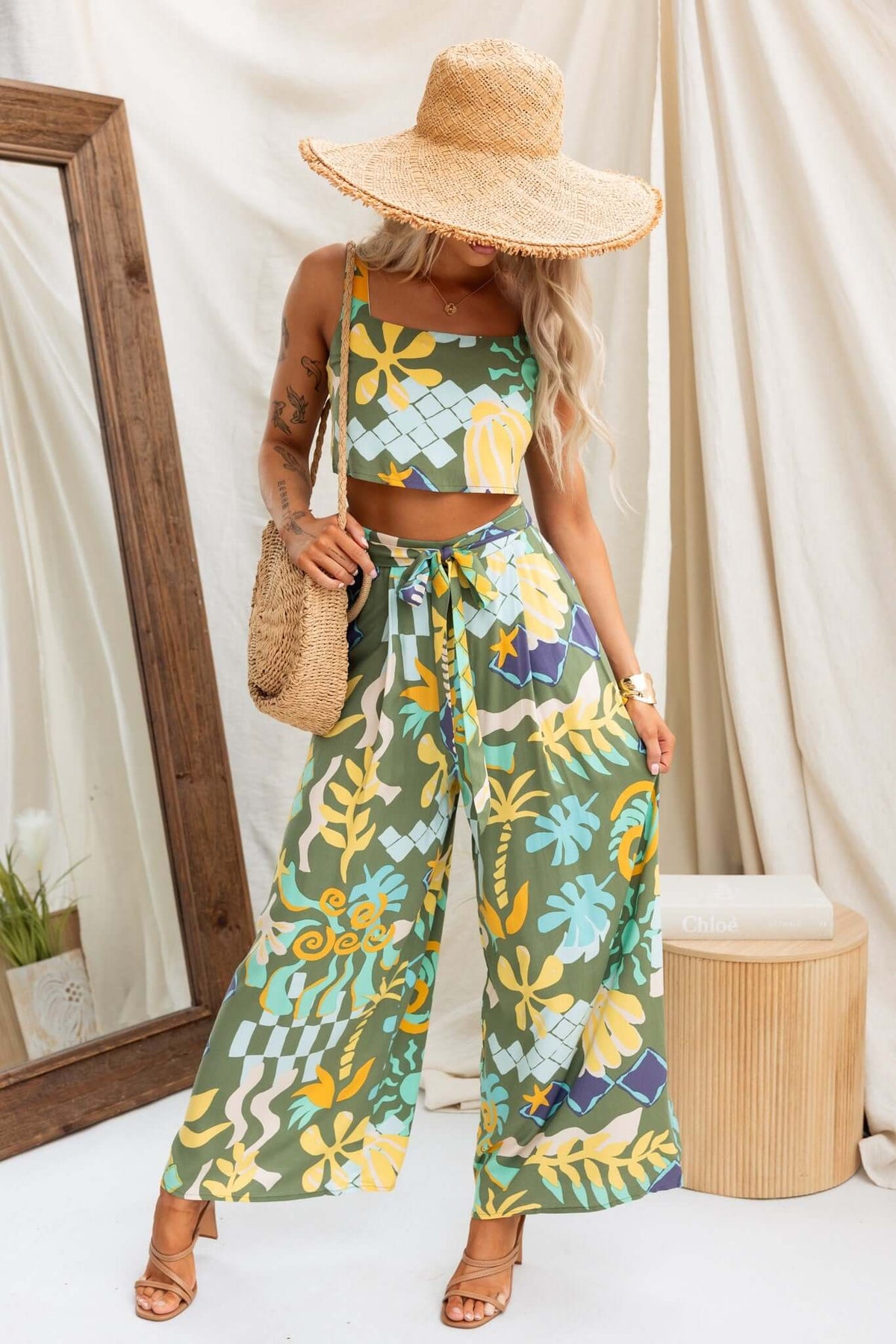 Woman in Warana Pants featuring a mid-high waist, colorful floral pattern, paired with a matching crop top and wide-brim hat.