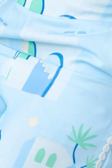 Close-up of the Uriela Top showcasing a light blue fabric with a playful, colorful print of buildings and greenery.