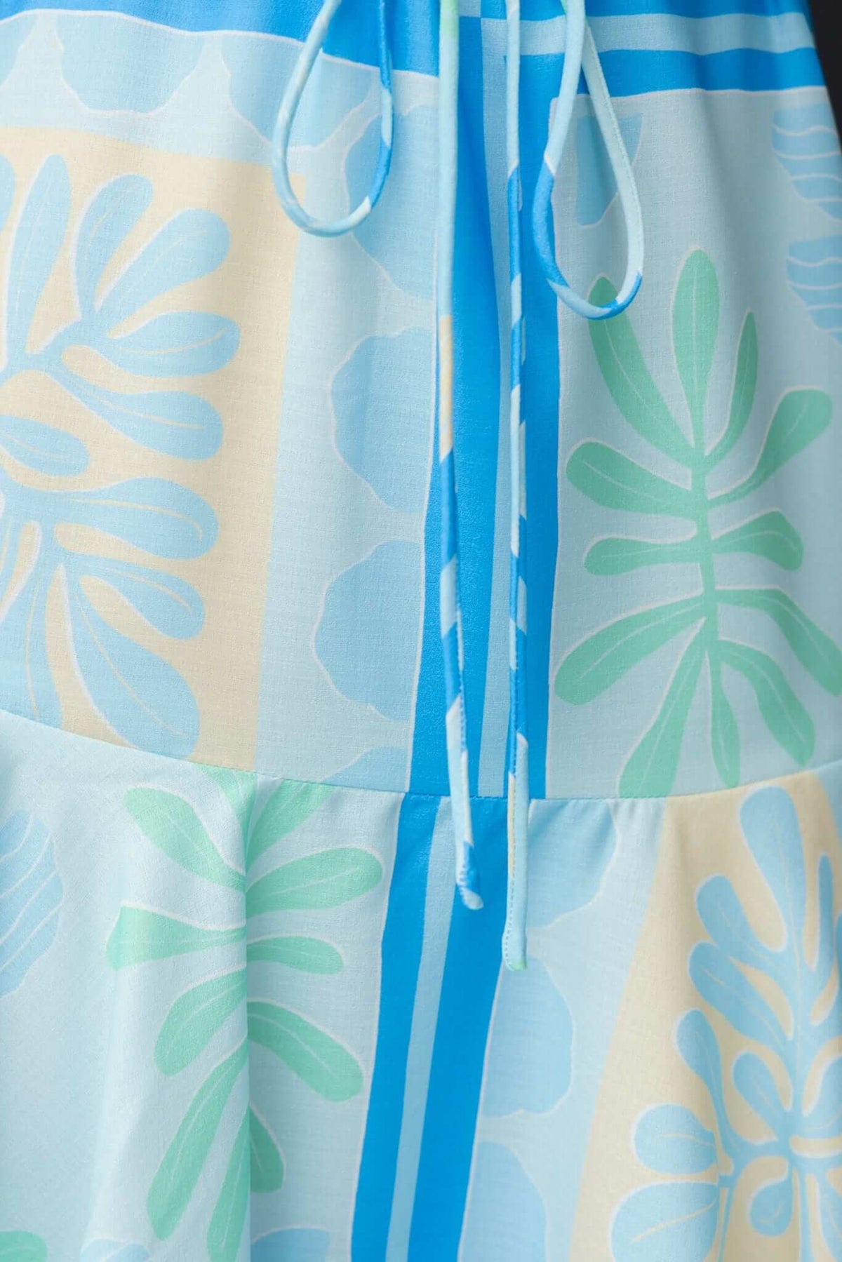Close-up of Monash Dress showing vibrant blue, green, and yellow pattern with removable tie detail.