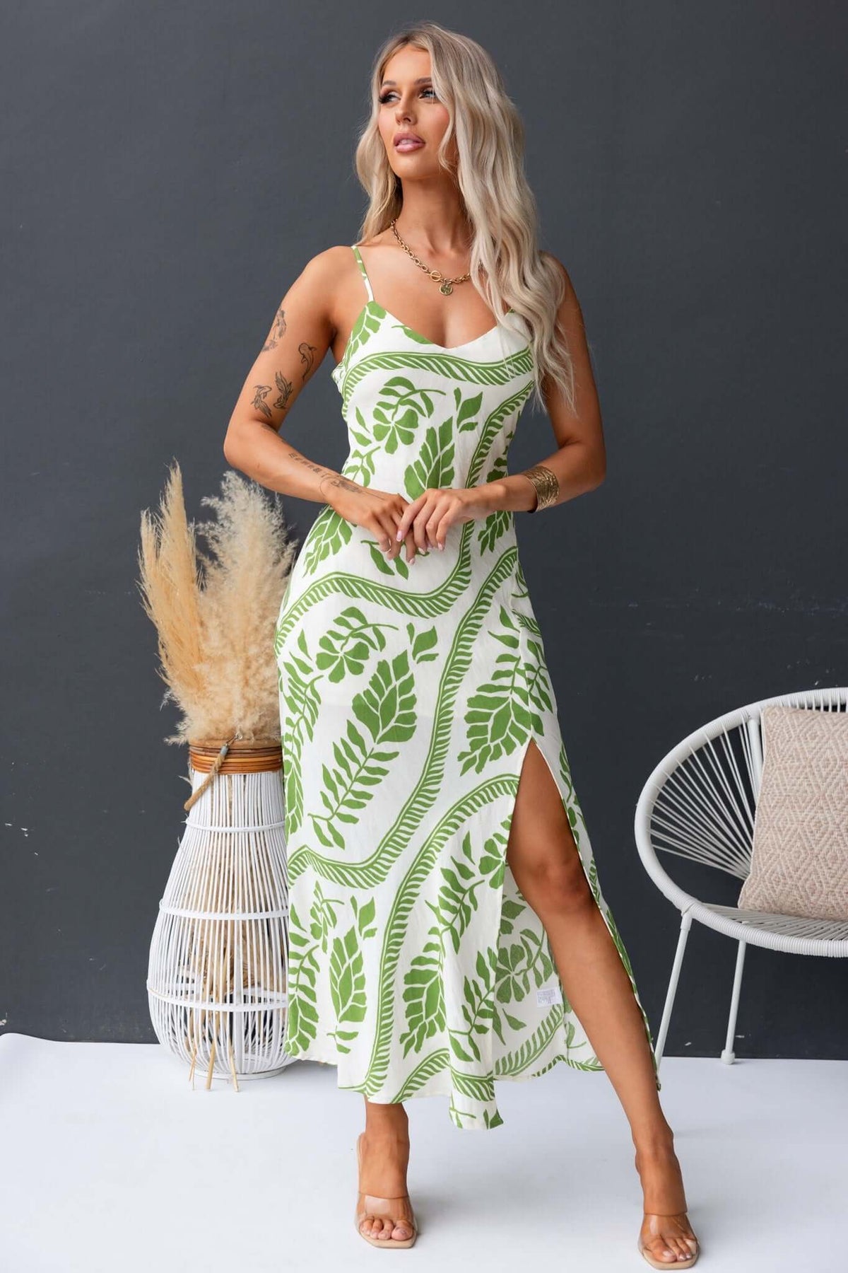 Kalinda Maxi Dress featuring adjustable straps, V-neckline, and front split, styled with greenery backdrop.