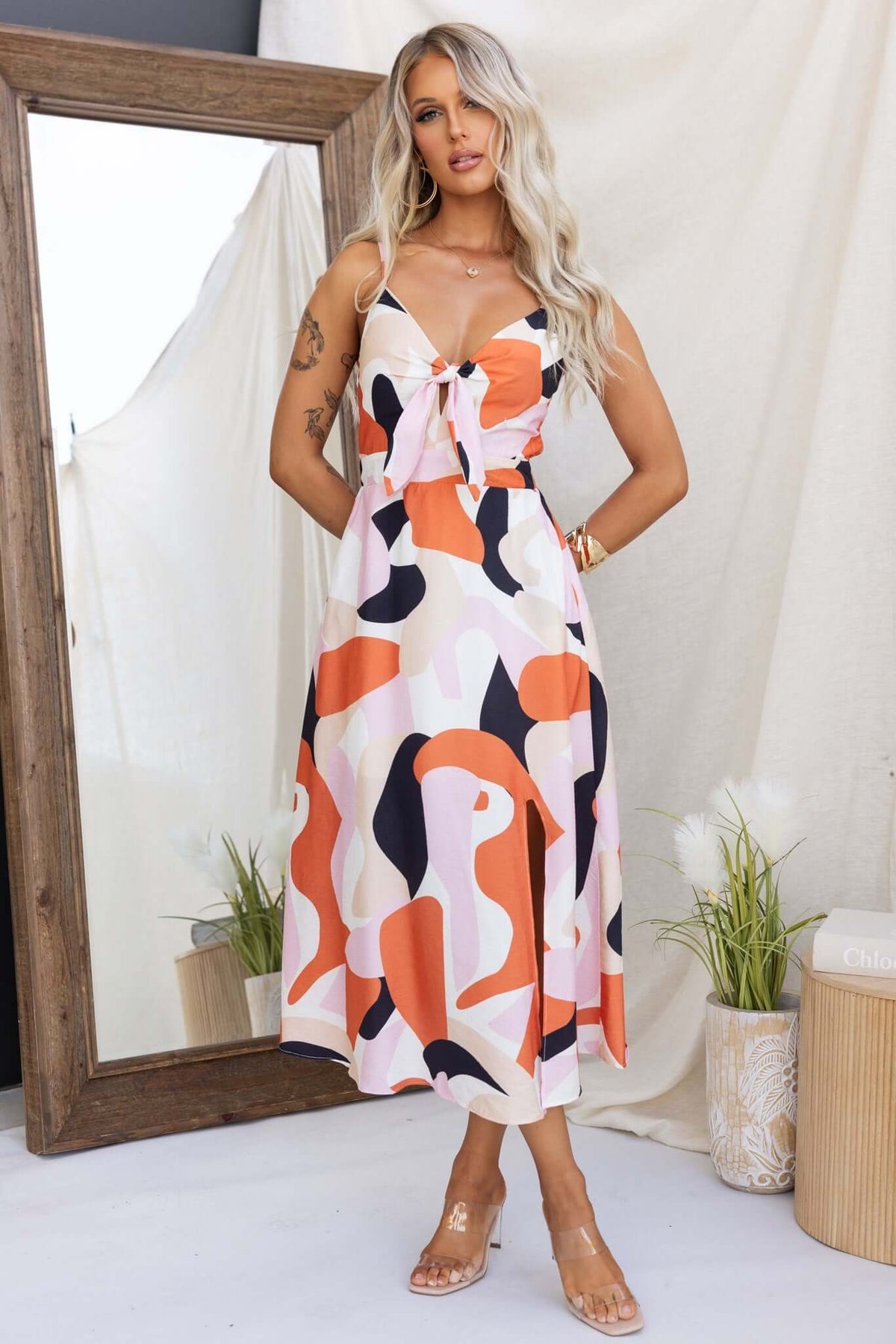 Modina Midi Dress with adjustable straps, colorful abstract print, and tied bust detail. Model showcases stylish summer wear.