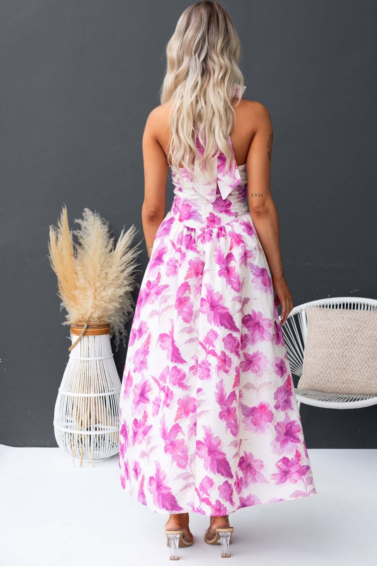 Back view of Imarnie Maxi Dress featuring tie neckline and floral print, styled with sandals against a neutral backdrop.