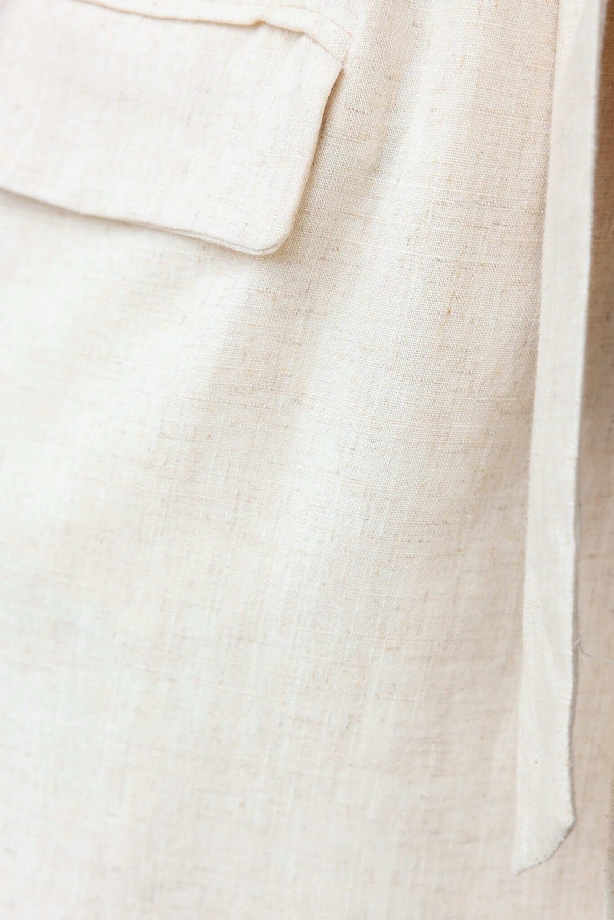 Close-up of Stowe Dress fabric featuring a faux pocket and tie detail in light beige, highlighting its soft texture.