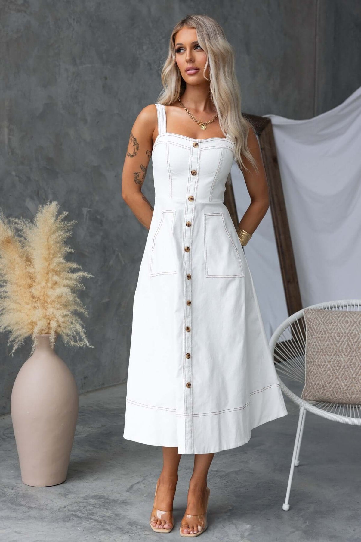 Model wearing a white denim midi dress with button details and pockets, styled for a modern look.