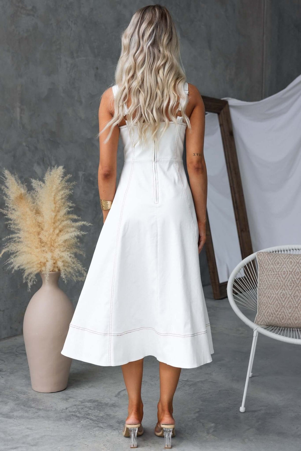 Back view of a woman in a white sleeveless midi dress with a fitted bodice and flared skirt, showcasing elegant style.