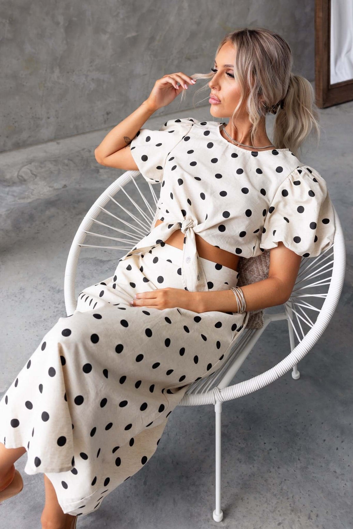 Woman in polka dot midi skirt and top, seated in a modern chair, showcasing stylish outfit design.