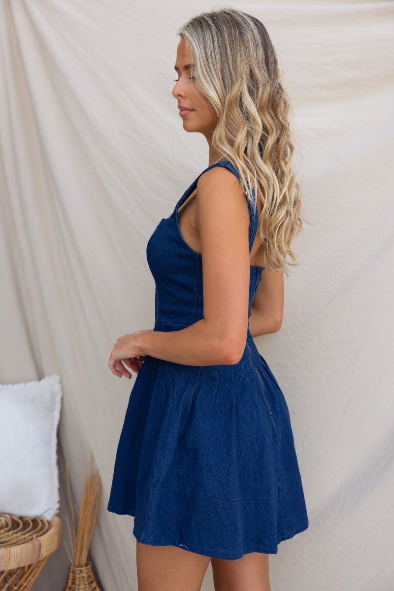 Side view of a woman wearing a Cannie Denim Dress, showcasing adjustable straps and a flared skirt design.