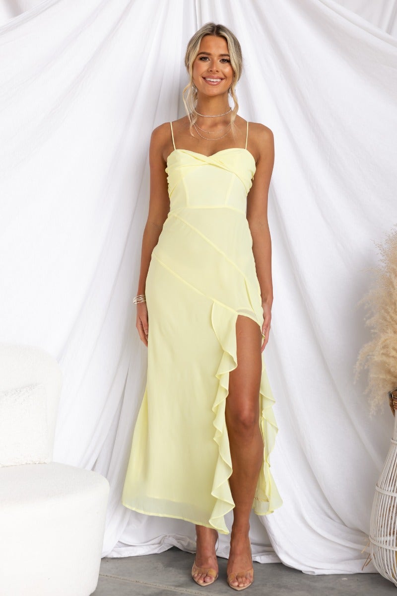 Cinzia yellow maxi dress with adjustable straps, twist detail, and ruffle trim, worn by model against a soft backdrop.