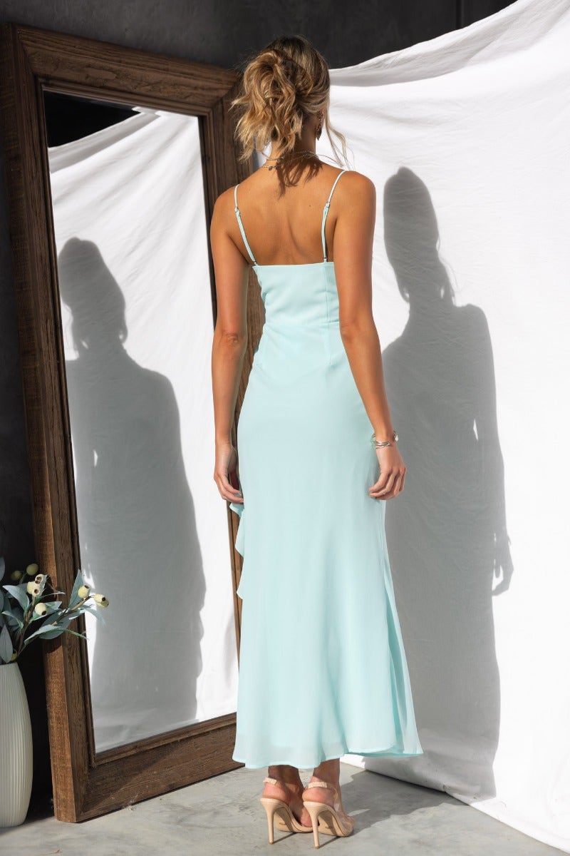 Back view of Cinzia Maxi Dress with adjustable straps and a ruffle trim, displayed in a stylish indoor setting.