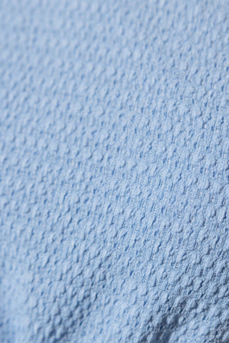 Close-up of textured blue fabric showcasing the intricate pattern, ideal for stylish tops.