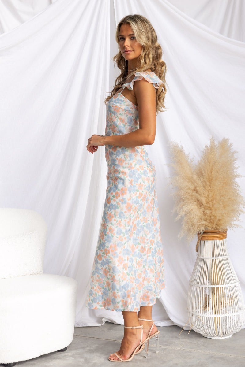Model wearing Kellana Midi Dress, a floral print midi dress with ruffle straps, styled with a minimalist backdrop.
