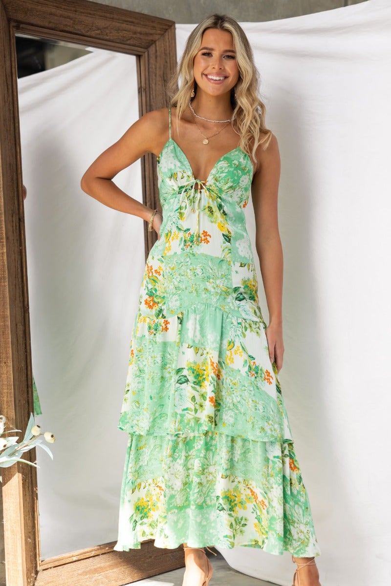 Model in a floral print Wildest Dreams maxi dress with adjustable straps and tie detail, standing in front of a mirror.