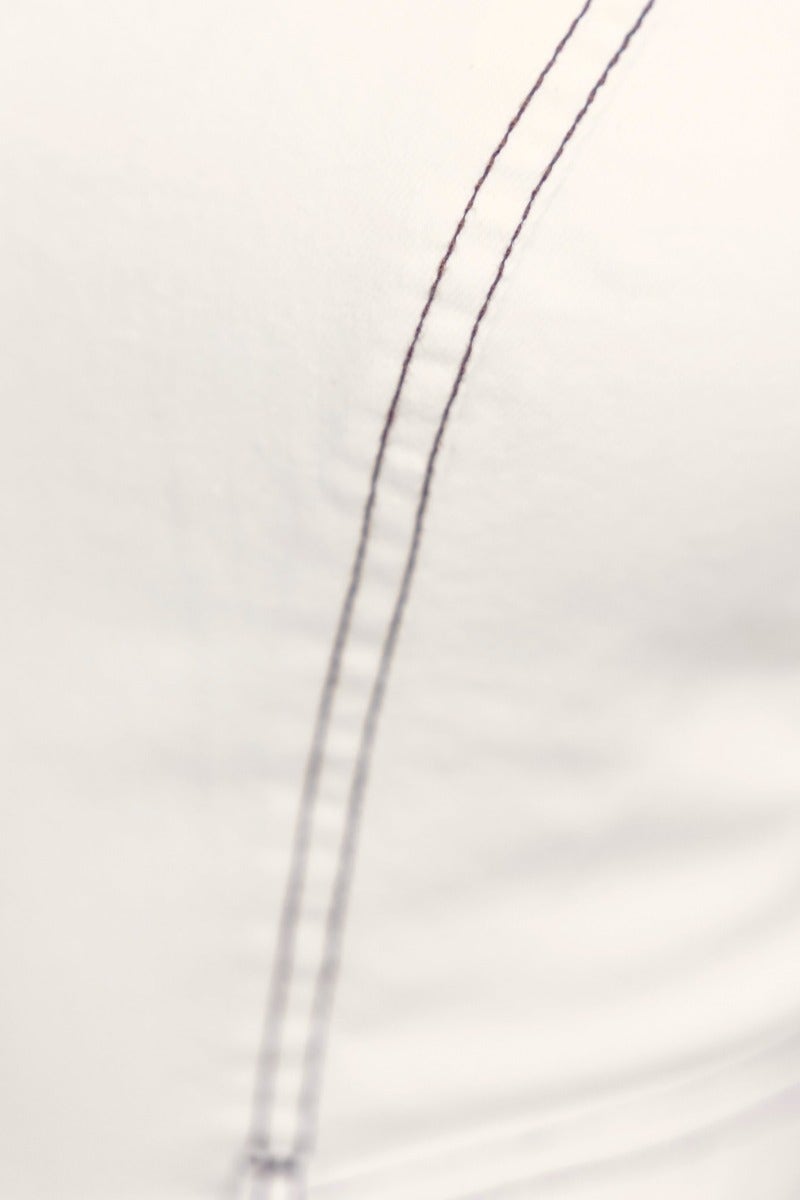 Close-up of stitching detail on a white denim fabric, highlighting texture and craftsmanship.