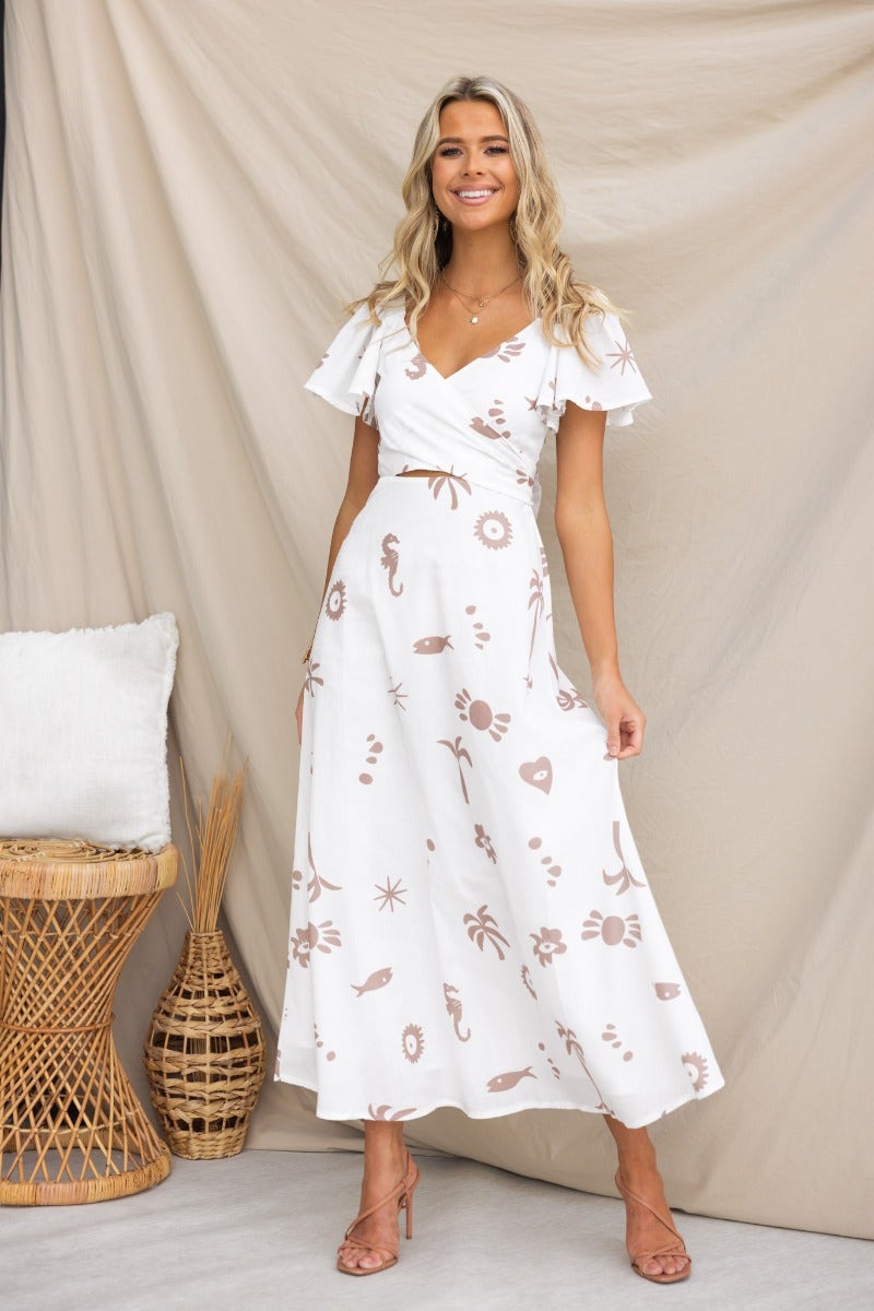 Fermina Wrap Maxi Dress featuring floral print, elastic sleeves, and wrap tie detail, styled with natural backdrop.