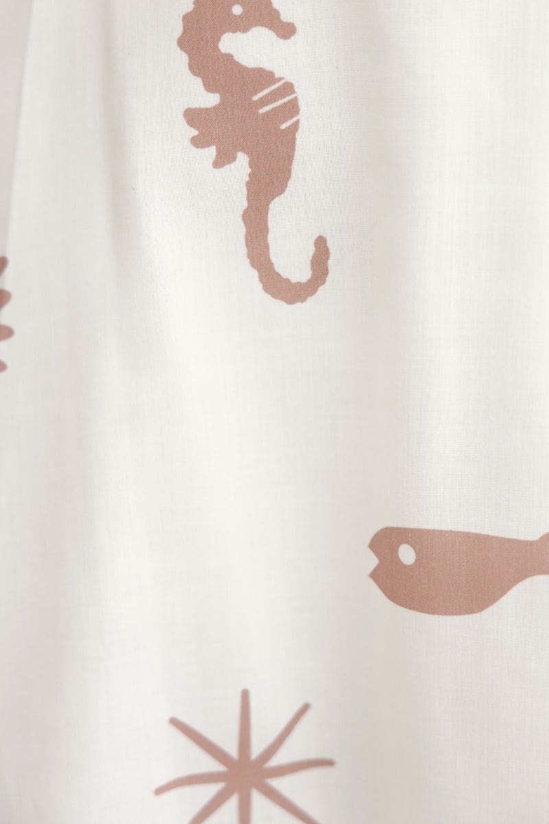 Close-up of a fabric featuring seahorse, fish, and starfish patterns in a soft beige on white background.