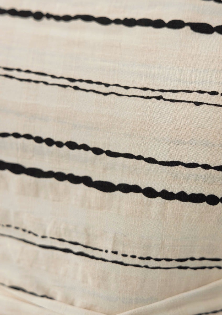 Close-up of a textured beige fabric with black stripes, showcasing the material of the Haiti Dress.