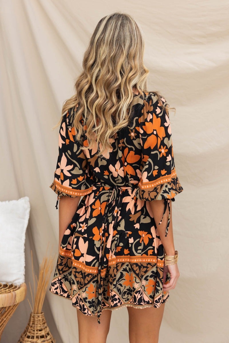 Back view of the Enver Dress featuring a black floral print, elastic cuffs, and tied waist detail.