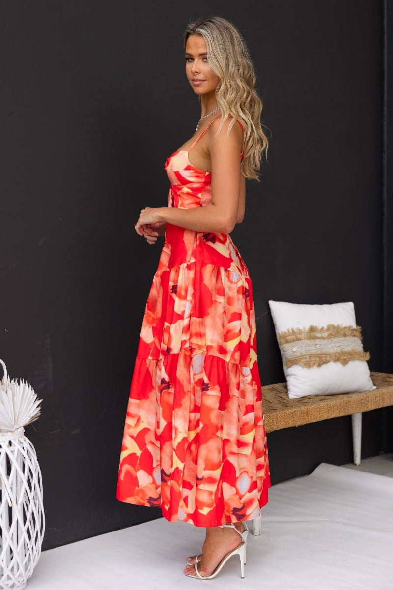 Model wearing Scorpio Maxi Dress with floral print, adjustable straps, and twist detail, showcasing a side view in a stylish setting.