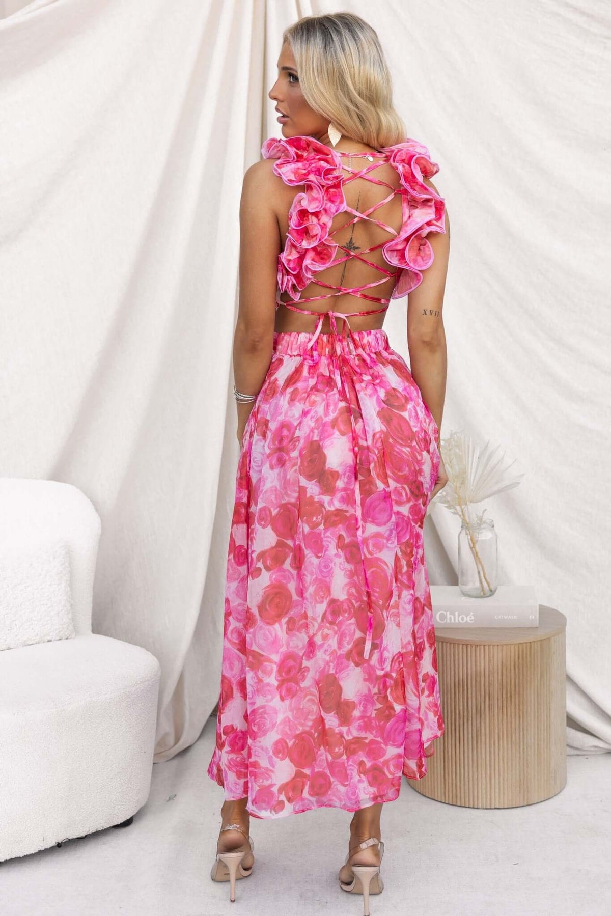 Back view of a woman in a pink floral Rosie Maxi Dress with ruffle straps and lace-up tie detail.