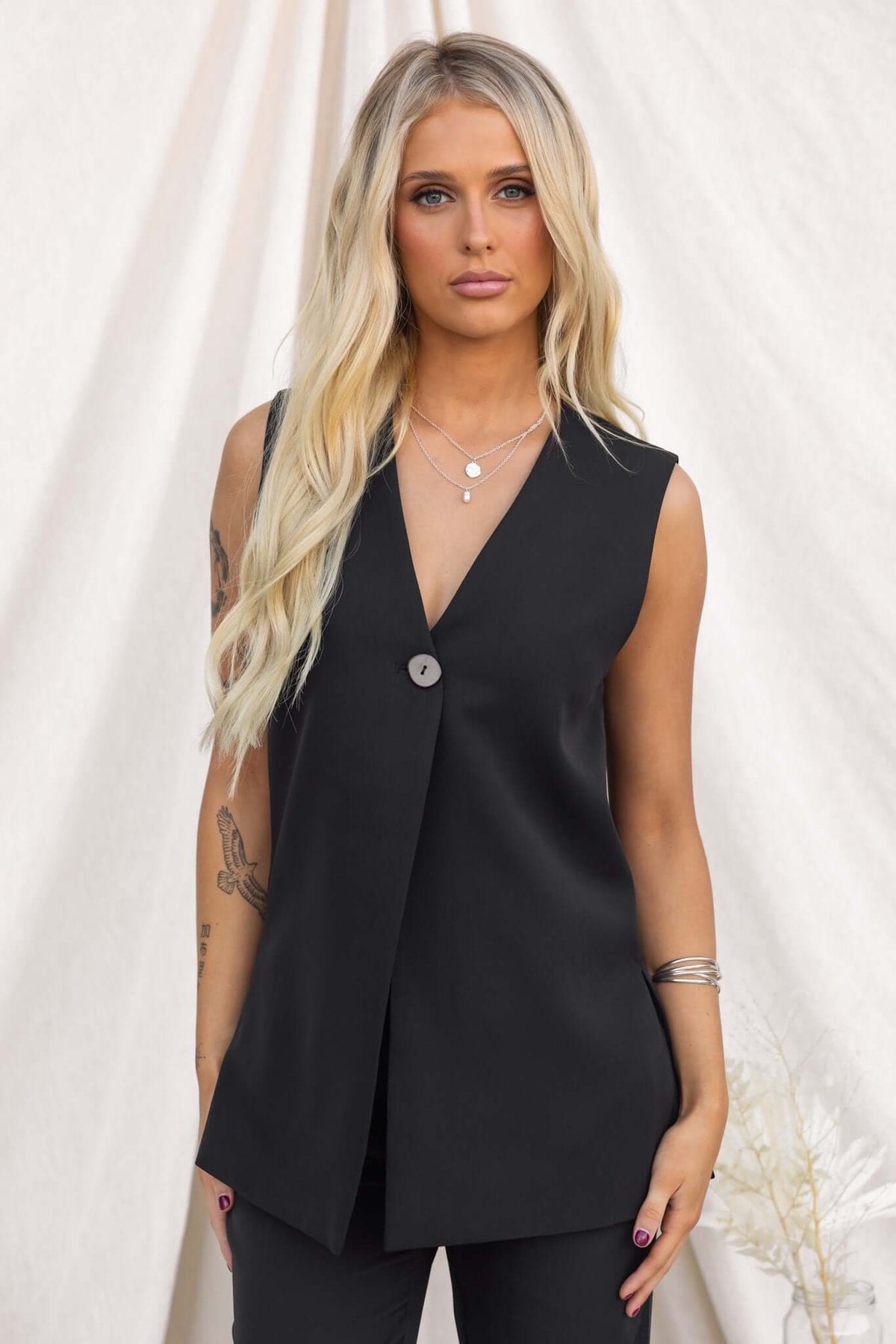 Ulani Top - Black vest with V-neckline and button, featuring side splits and a slightly relaxed fit.