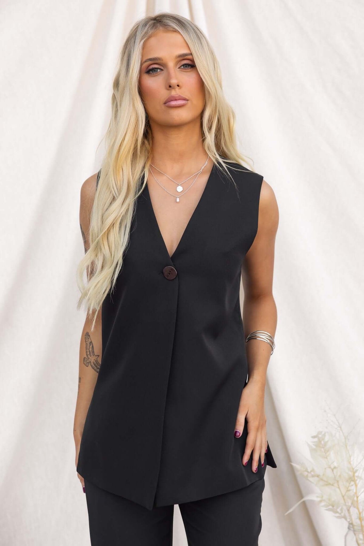 Model wearing the Ulani Top, a black vest with a V-neckline and button closure, styled for a relaxed look.