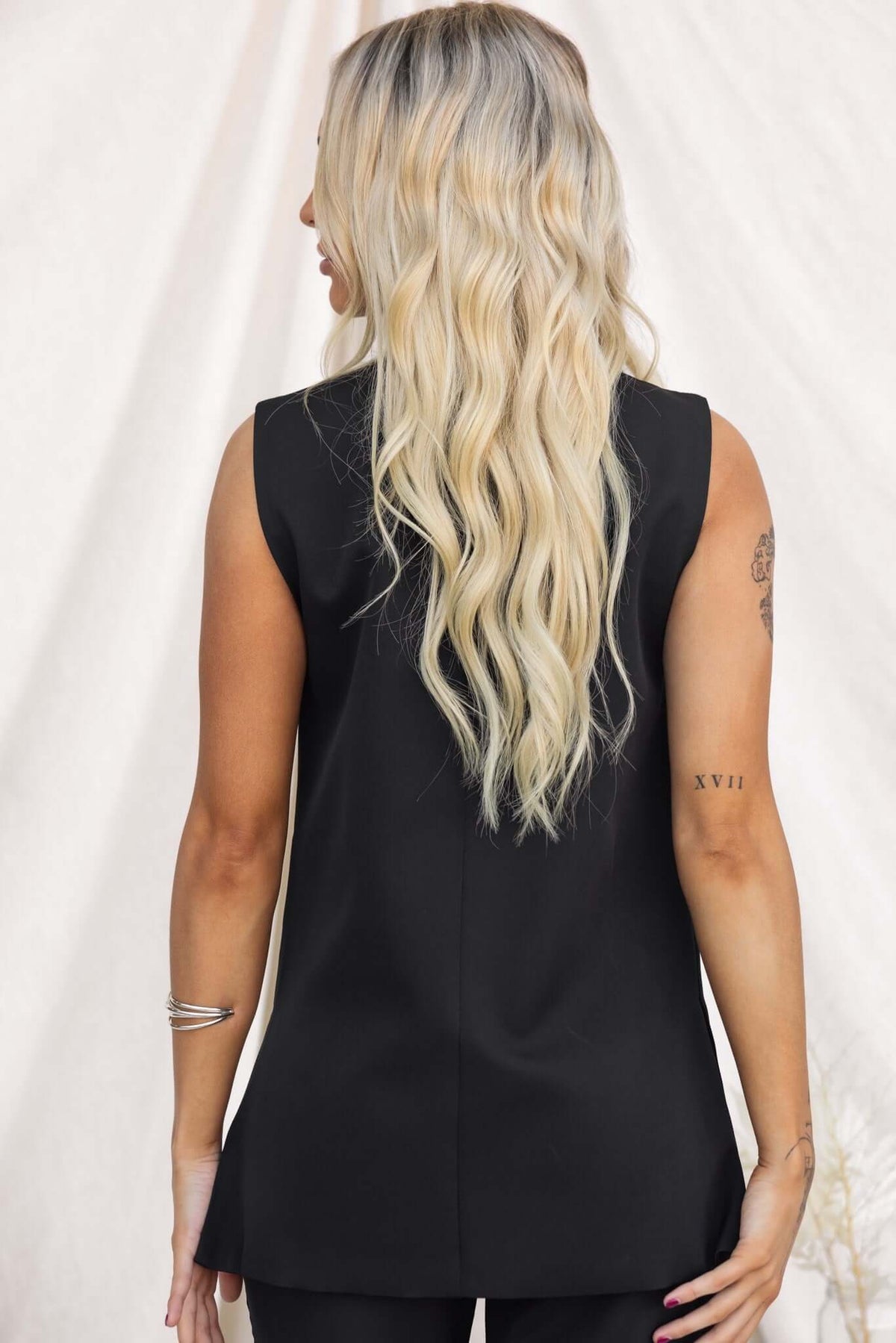 Back view of a woman wearing a black Ulani Top, featuring a sleek vest design and a slightly relaxed fit.