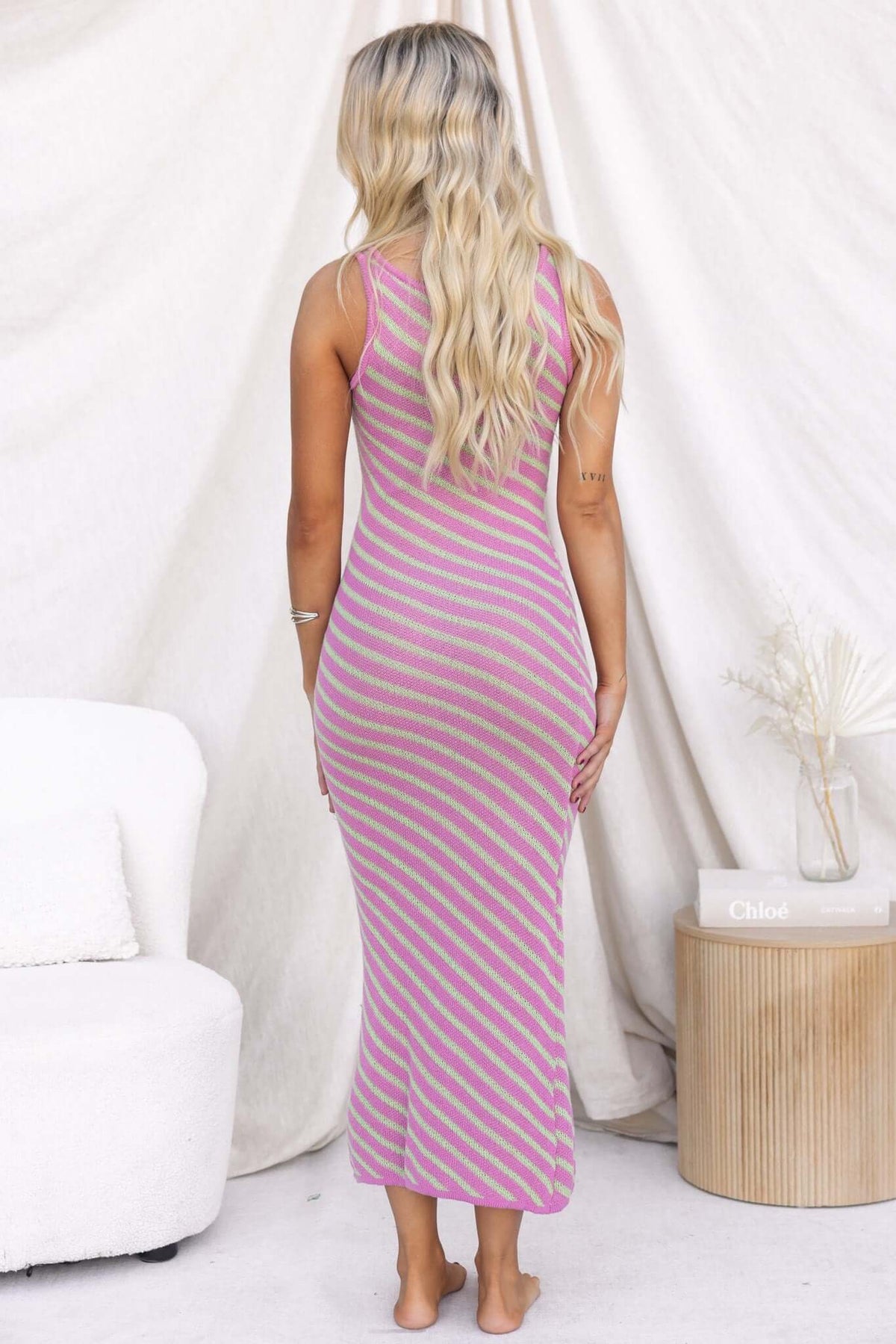 Back view of a woman in a striped pink and green Island Maxi Dress, showcasing a scoop neckline and fitted style.