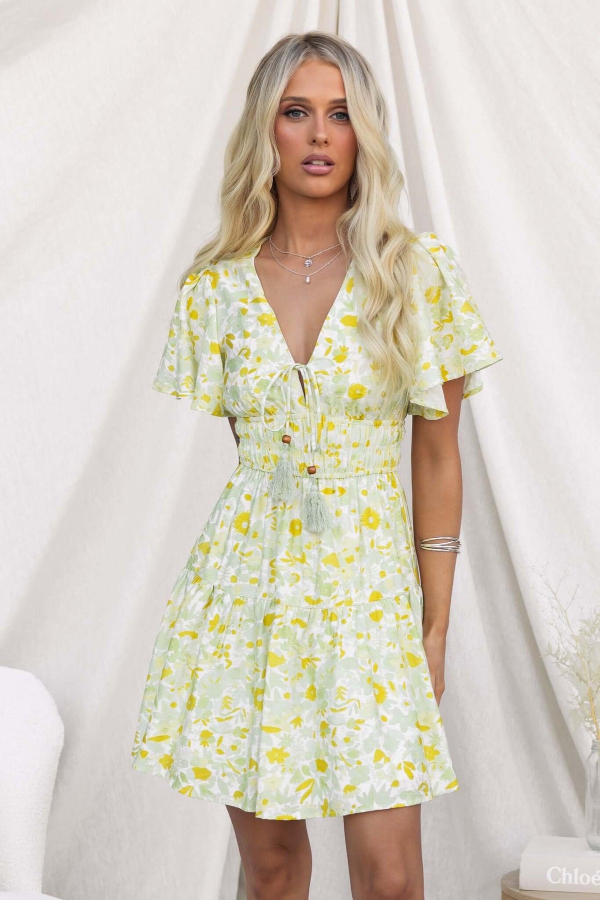 Isha Dress featuring a V-neckline, tie at bust, and floral pattern in yellow on a light background.
