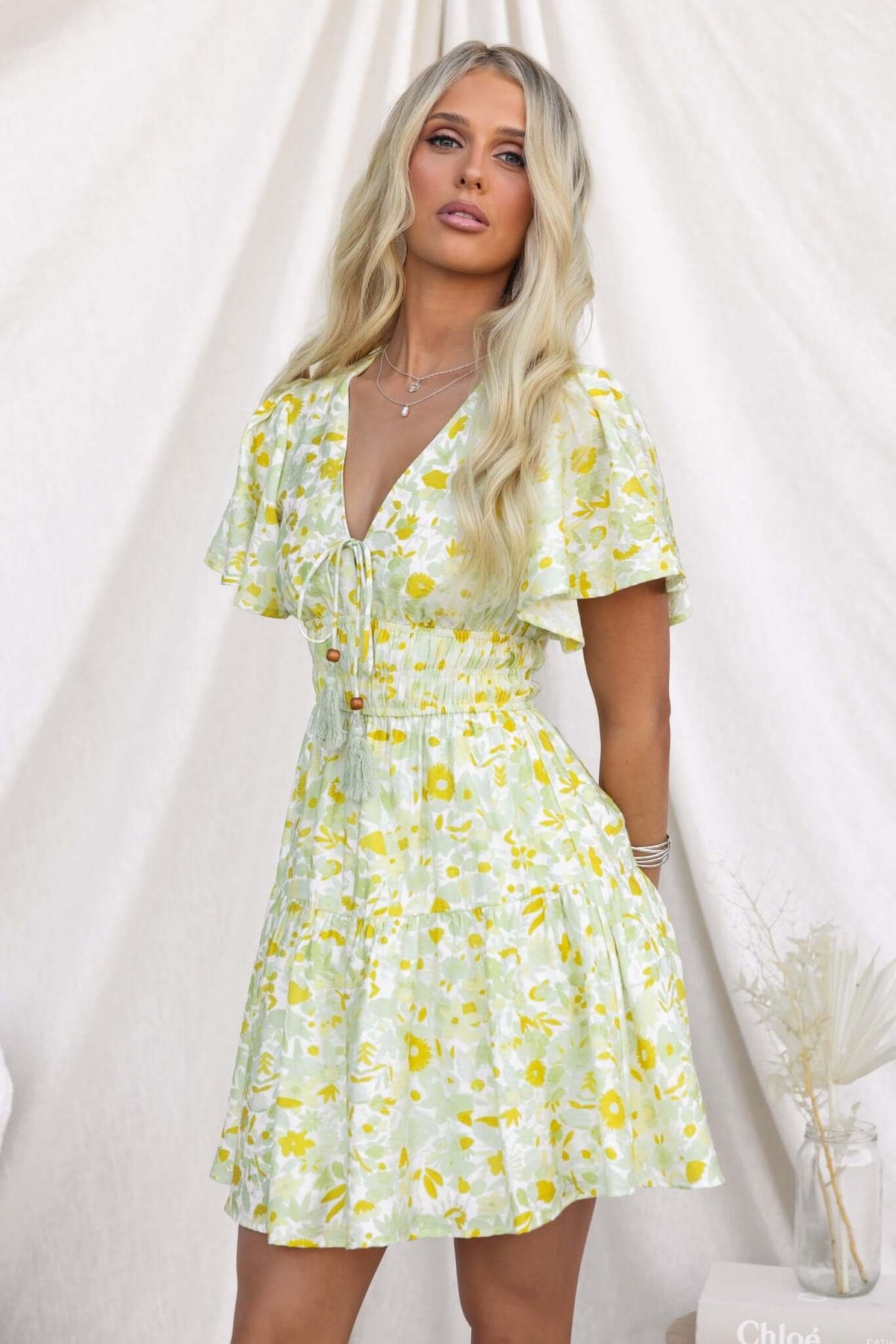 Isha Dress featuring a V-neckline, tie at bust, and elastic waistband, perfect for a summer look.