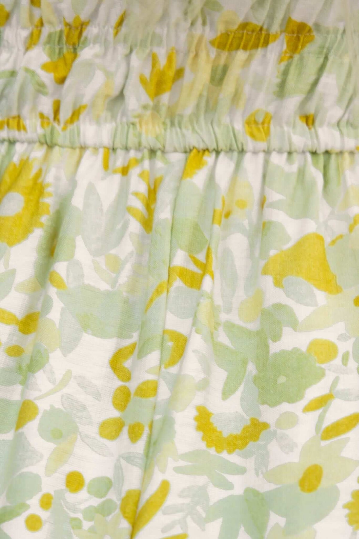 Close-up of Isha Dress fabric featuring delicate green and yellow floral print with gathered elastic waistband.
