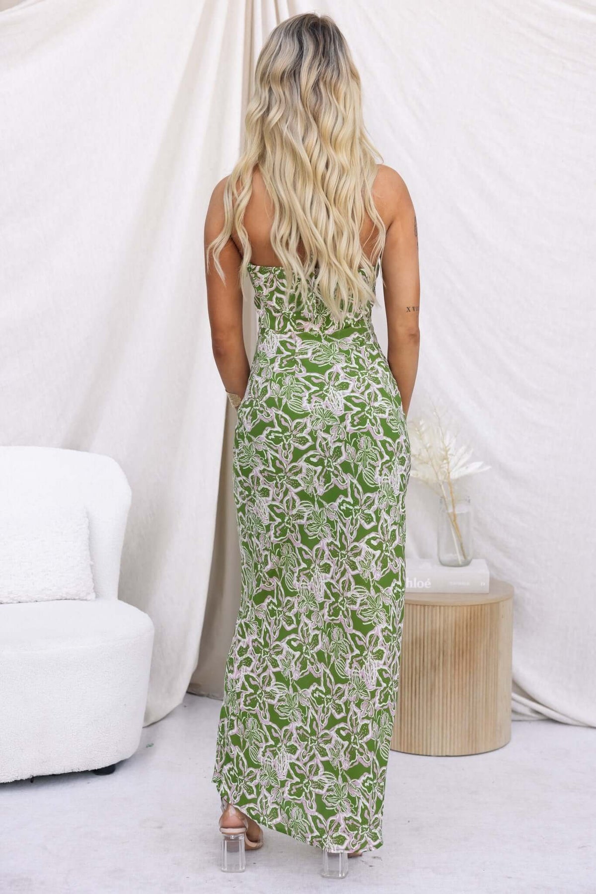 Back view of a woman wearing a green floral Nino Maxi Dress with adjustable neckline in a stylish setting.