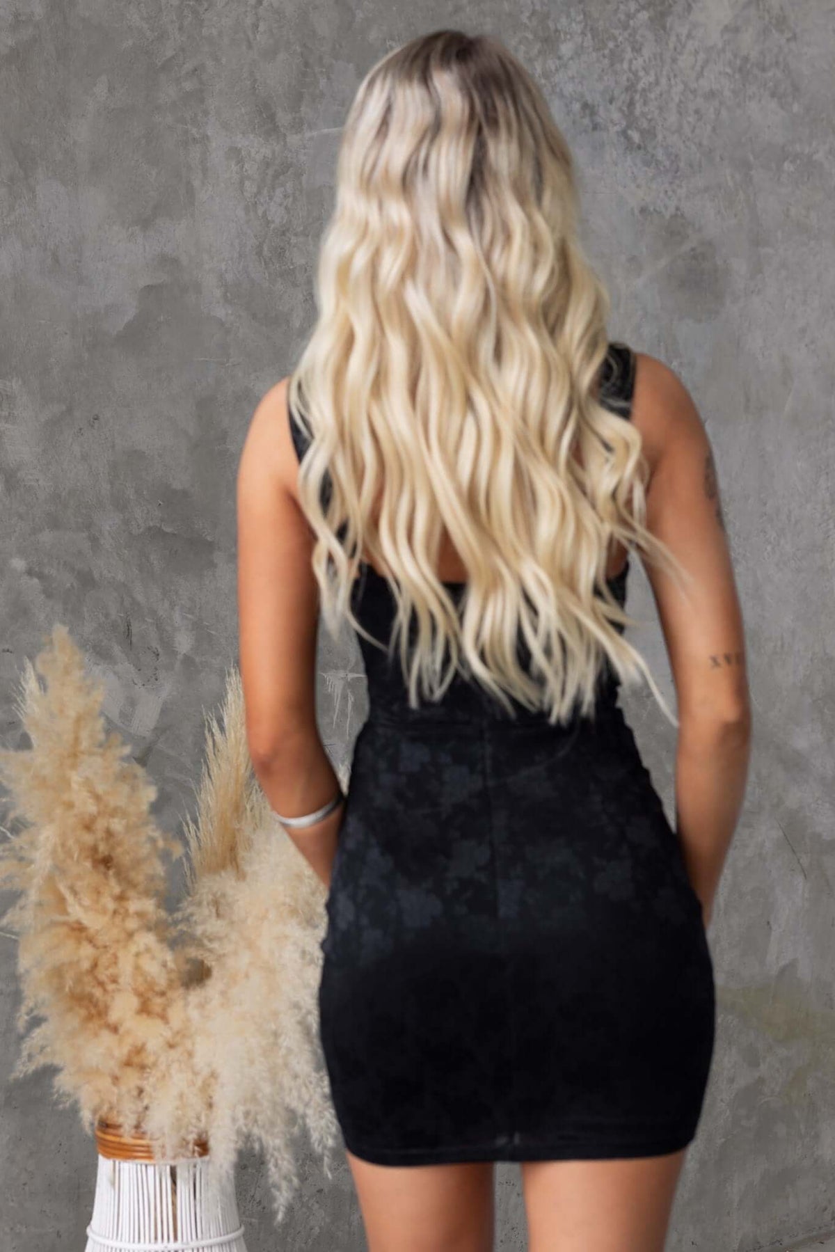 Back view of a woman in a black stretchy dress with adjustable straps, showcasing a sleek silhouette.