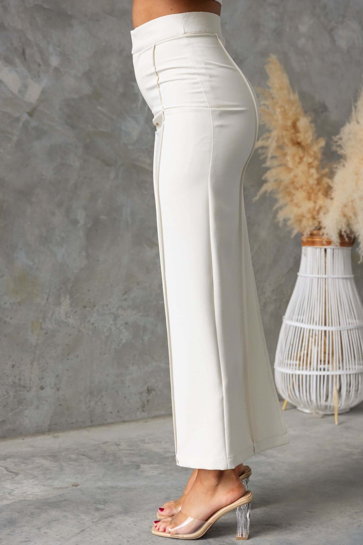 Side view of Jayne Maxi Skirt in cream, featuring a mid-high waist and back split, styled with transparent heels.