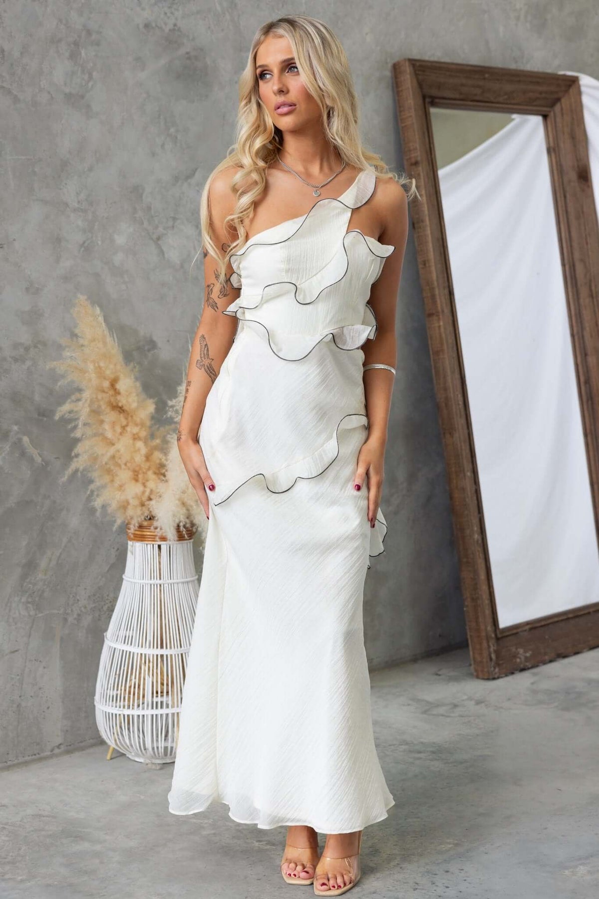 Elegant one-shoulder white maxi dress with ruffles and cut-out waist, styled for a chic look.
