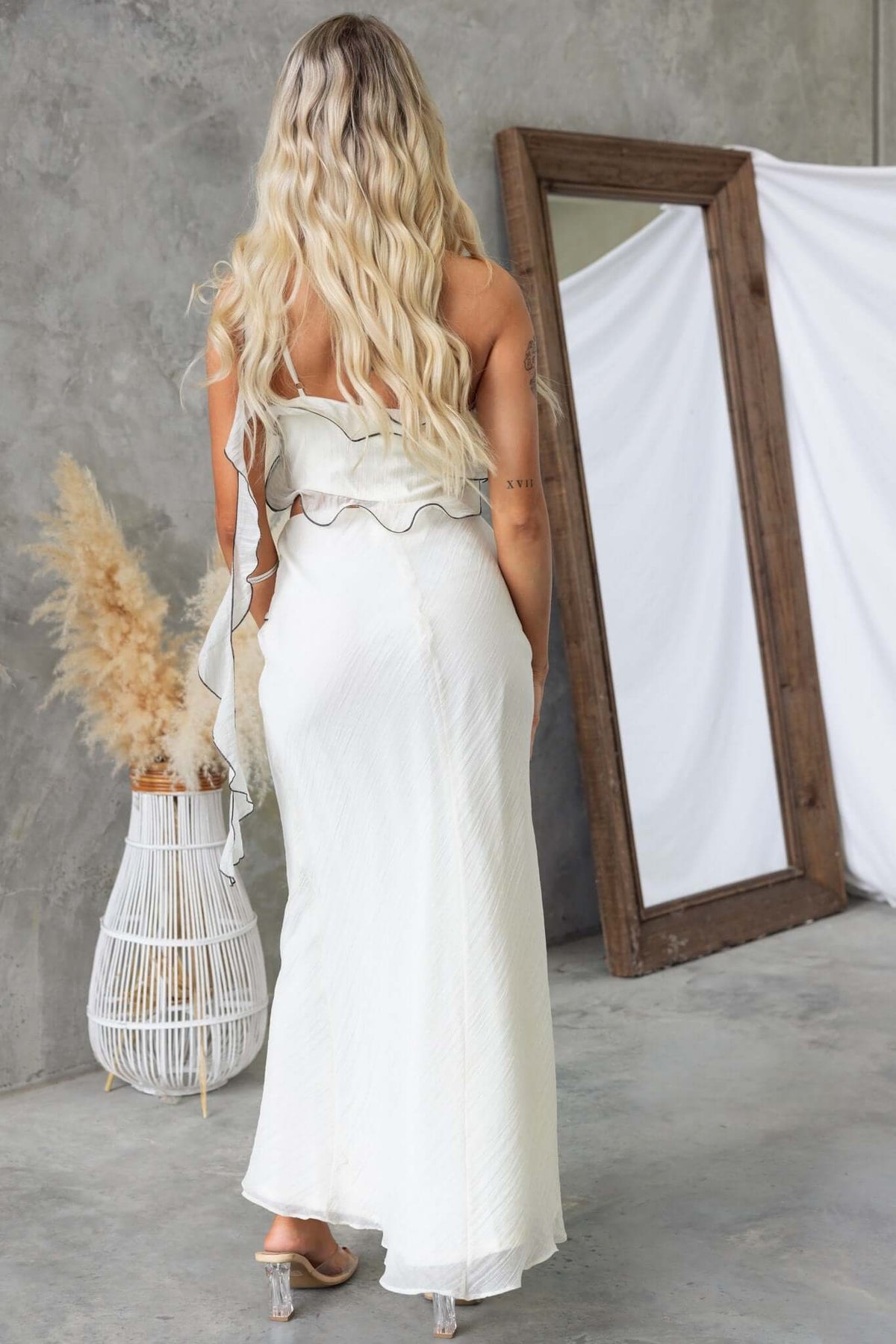 Back view of a woman in a clouded maxi dress with a one-shoulder neckline, showcasing textured fabric and elegant silhouette.