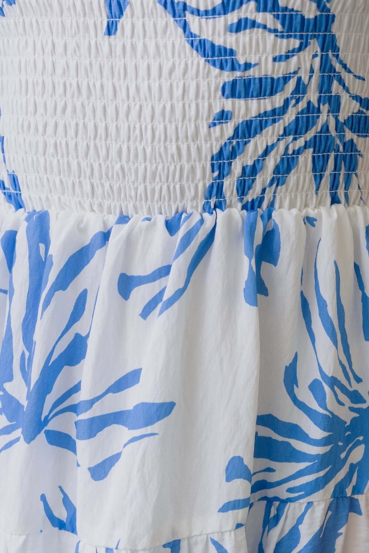 Close-up of the Blue Palms Dress featuring a shirred bodice and blue tropical print on a white background.
