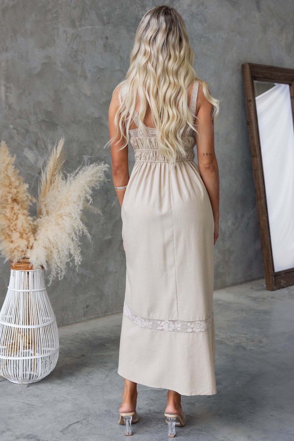 Back view of Eletti Midi Dress featuring lace detailing, elastic waist, and a neutral color against a concrete backdrop.