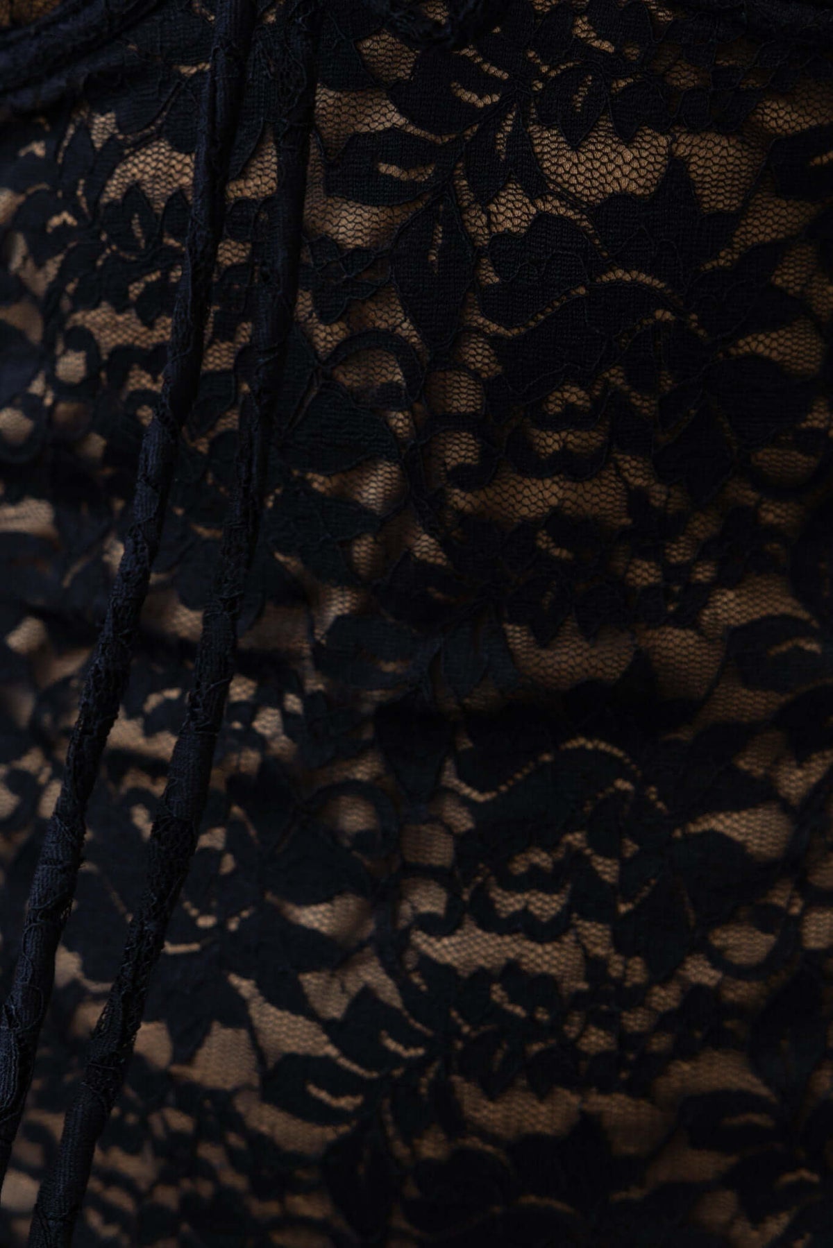 Close-up of intricate black lace fabric with floral patterns, showcasing the material of the Roswell Dress.