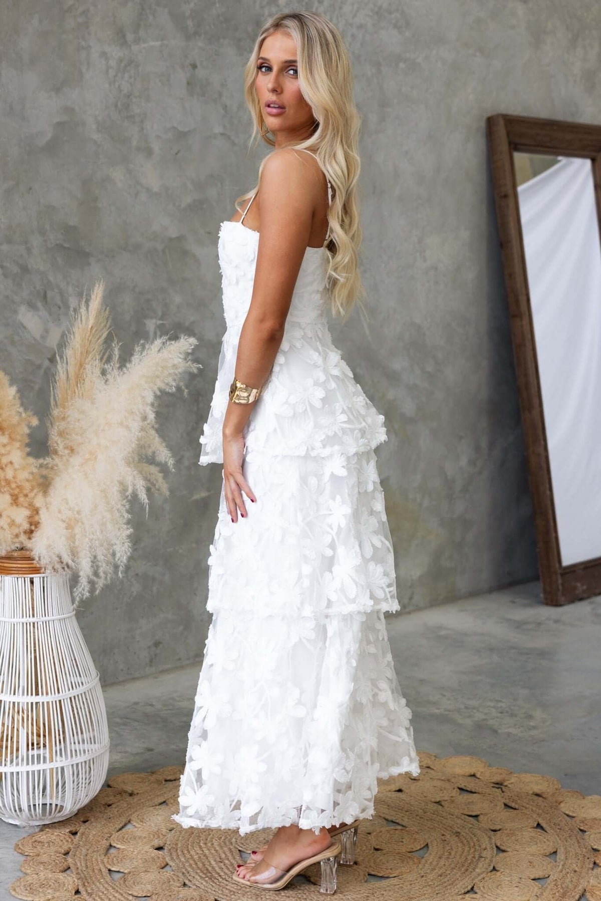 Woman in a white lace Jeannette Maxi Dress with adjustable straps, styled with accessories and a natural backdrop.