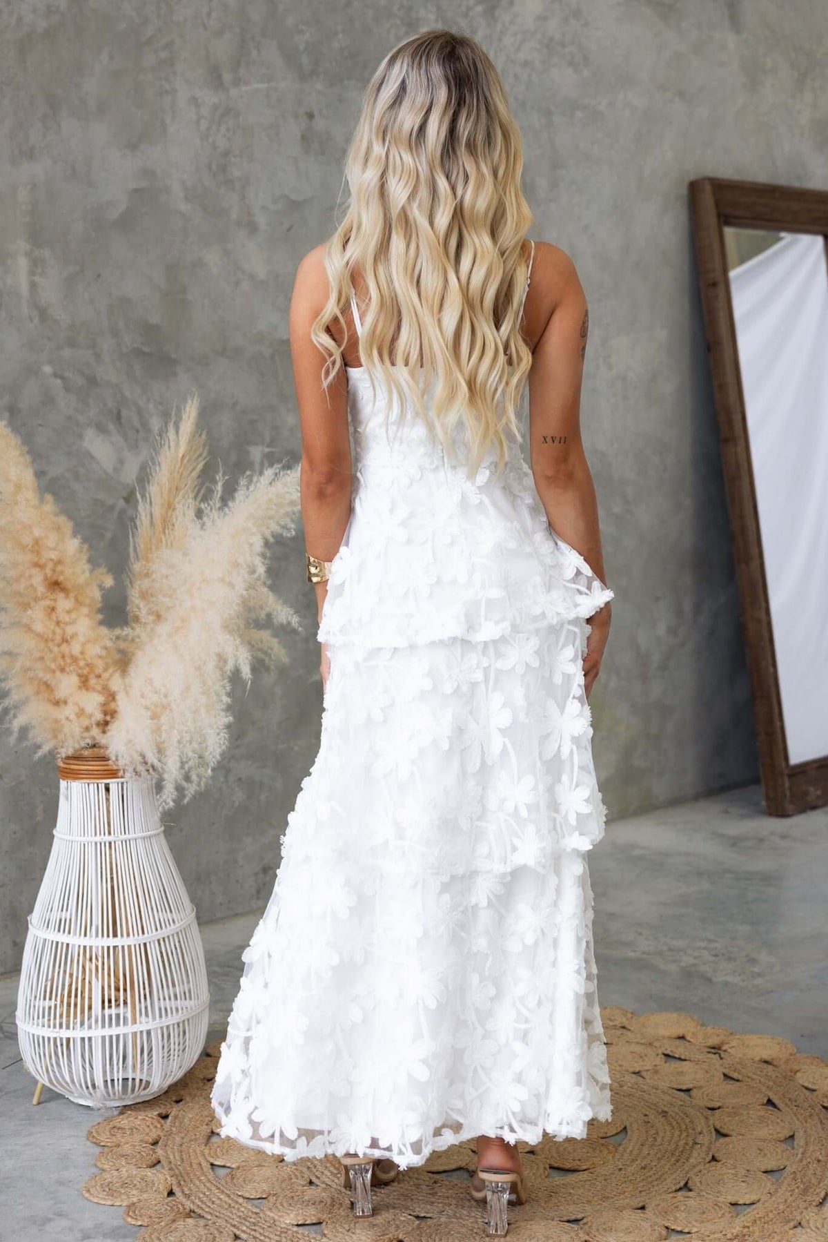 Back view of a woman in a white Jeannette Maxi Dress with lace detail, styled with wavy hair.