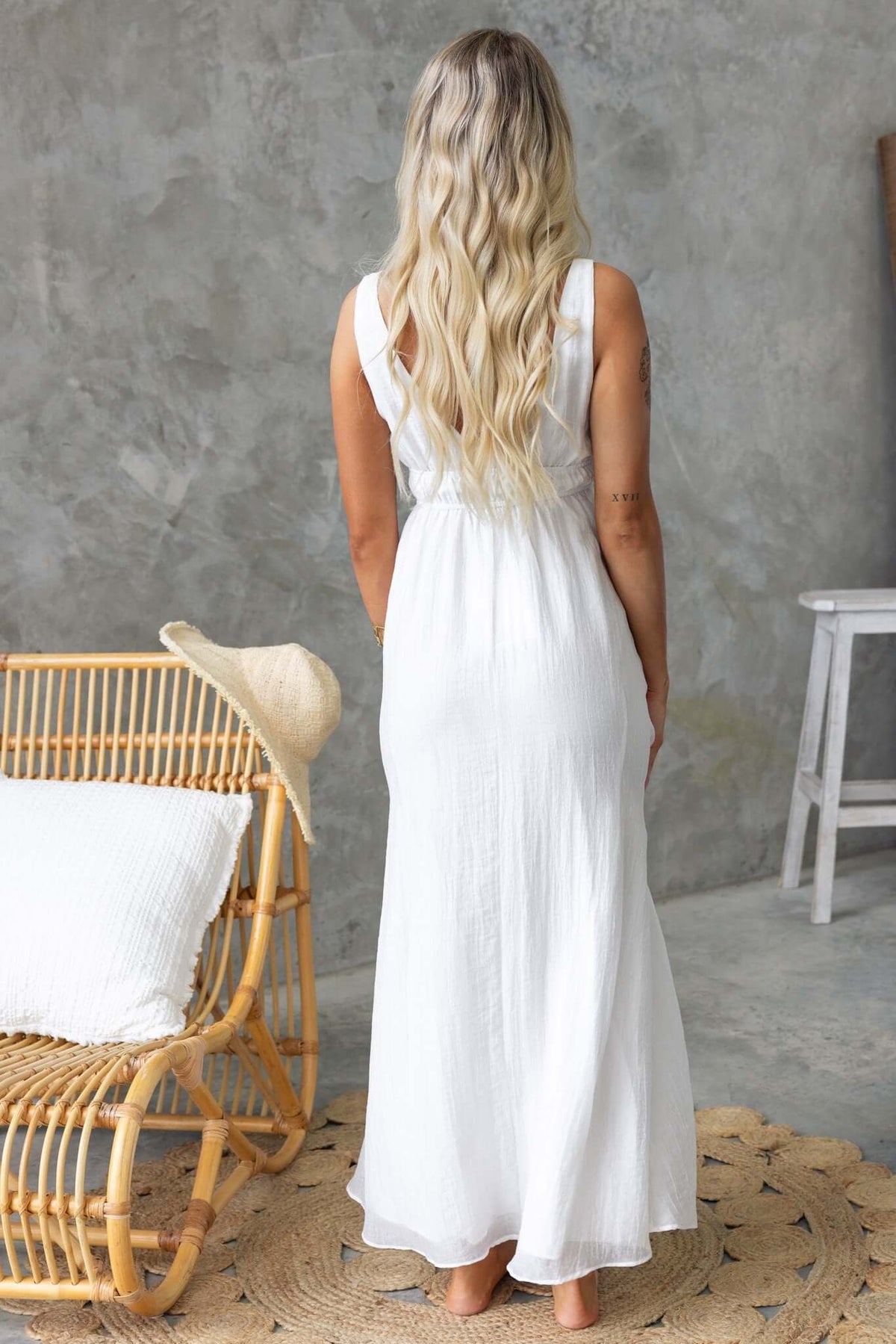 Back view of a woman in a white Keedan maxi dress with a V-neckline and elastic waistband, styled in a cozy indoor setting.
