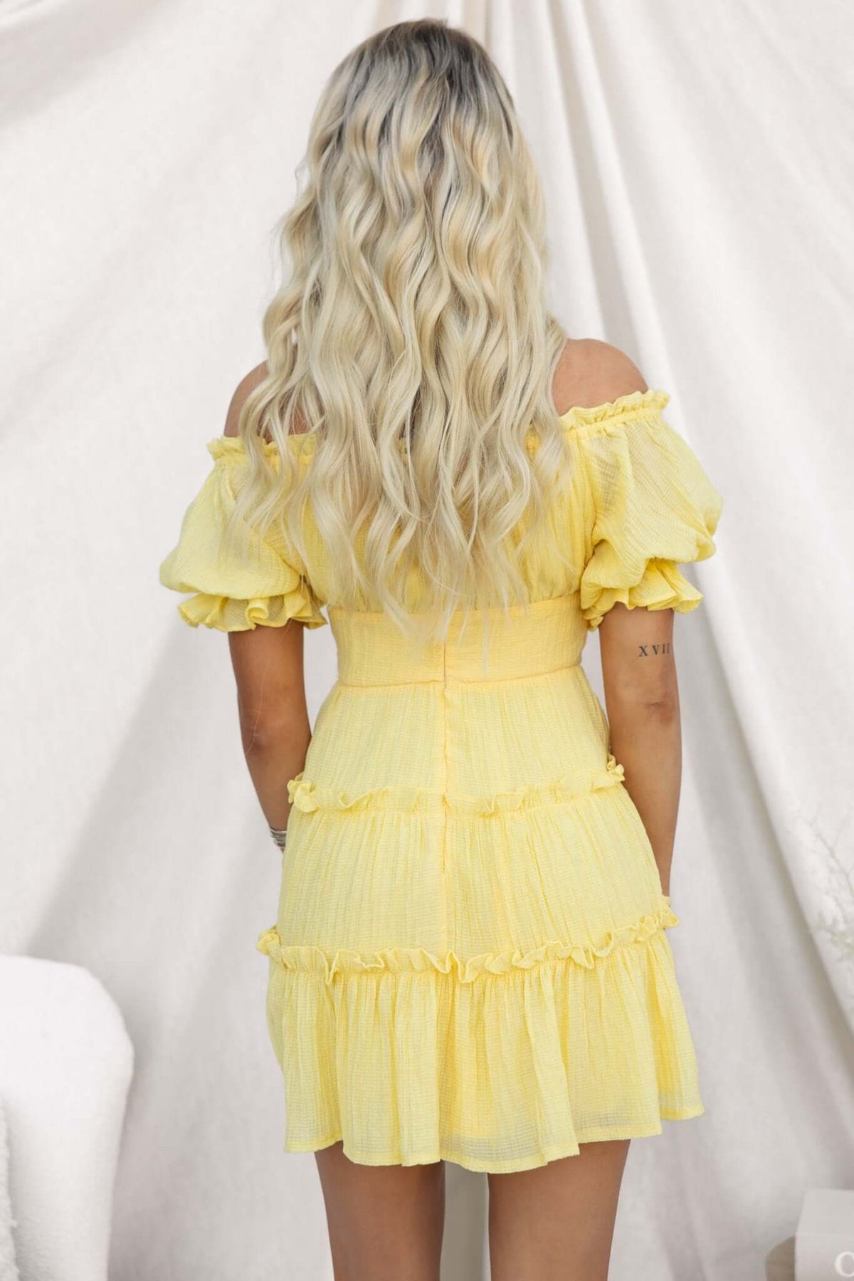 Back view of a textured yellow dress with off-shoulder neckline and ruffle details, showcasing a stylish look.