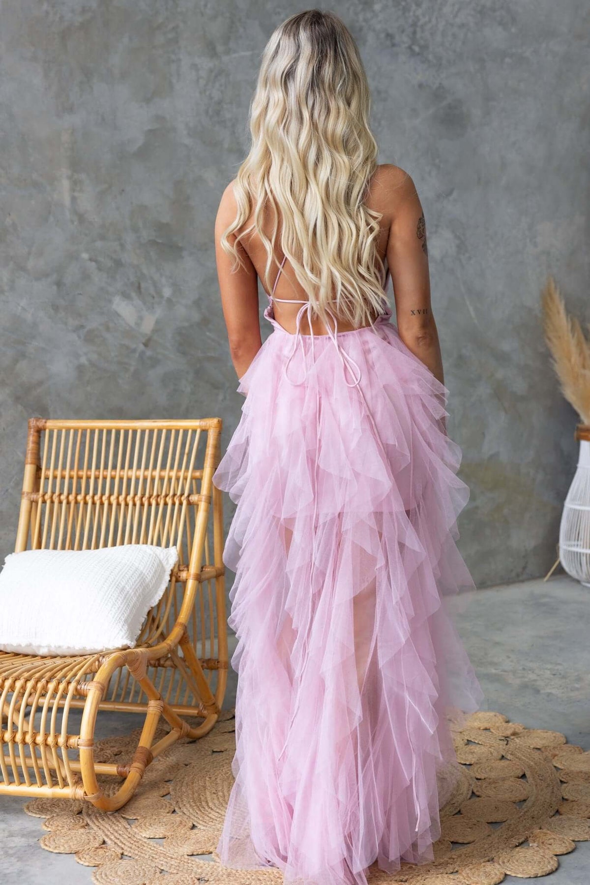 Model in a pink tulle maxi dress with back lace-up detail, showcasing ruffles and a flowing design.