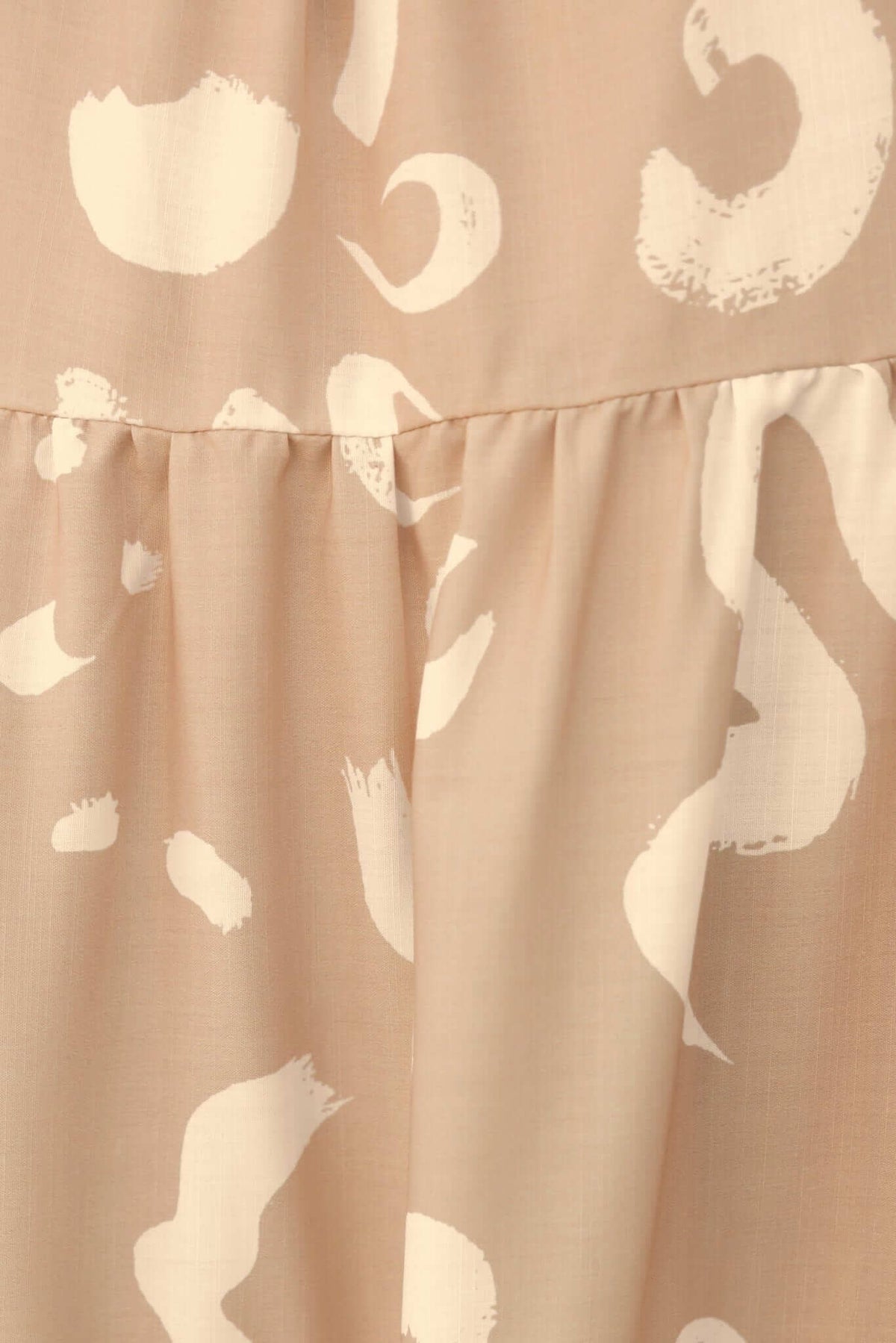 Close-up of Udelia Maxi Dress fabric featuring a beige background and white abstract pattern with gathered detail.